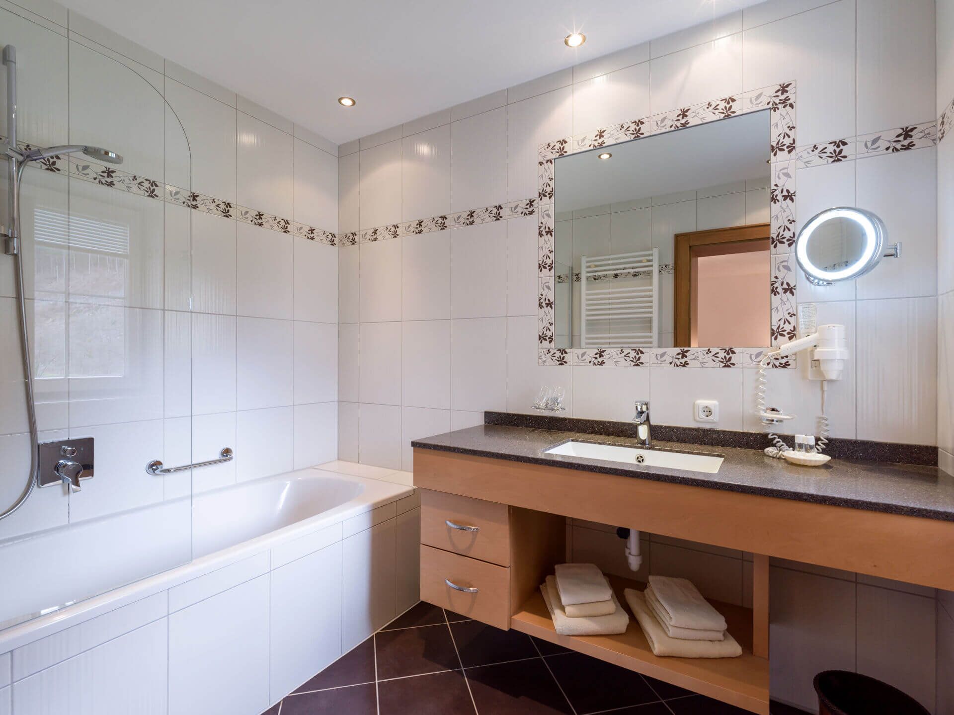 A modern bathroom with a bathtub, a sink with a vanity, a mirror with a floral border, and a shower.