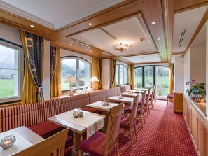 A dining area with tables and benches, large windows with curtains, and a chandelier. - Ferienhof Oblasser (Mayrhofen)