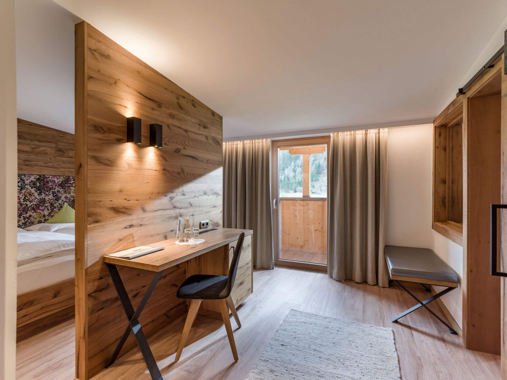 Une chambre moderne avec un bureau en bois, une chaise et un lit doté d’une tête de lit à motifs floraux.