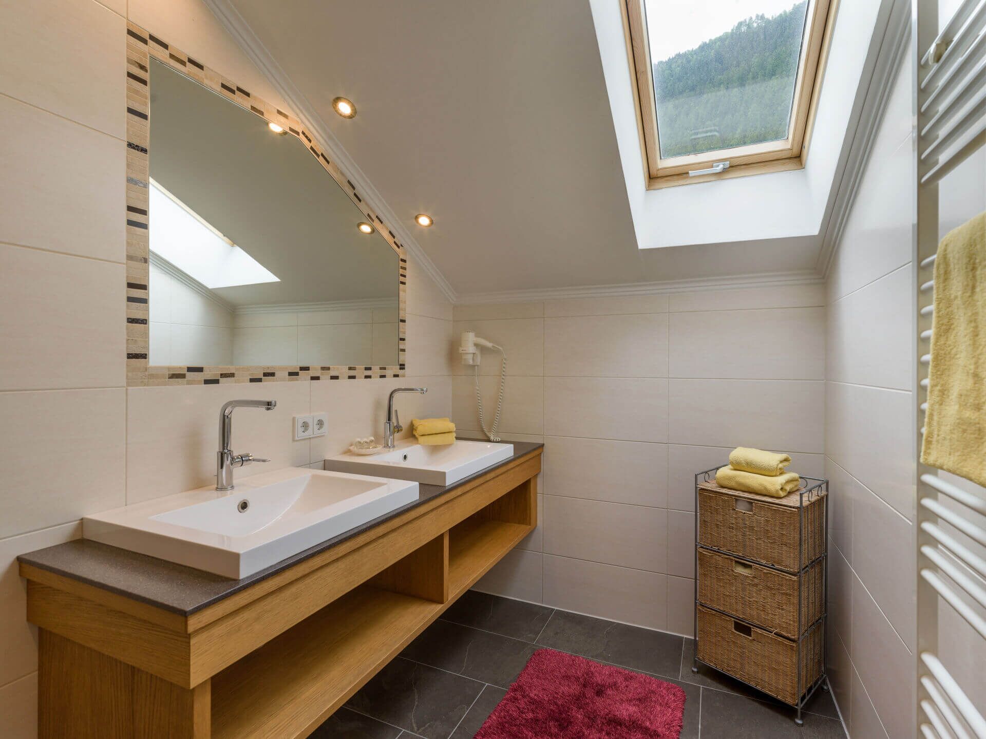 Une salle de bain moderne dotée d’une lucarne, de deux lavabos, d’un miroir et d’un porte-serviettes.