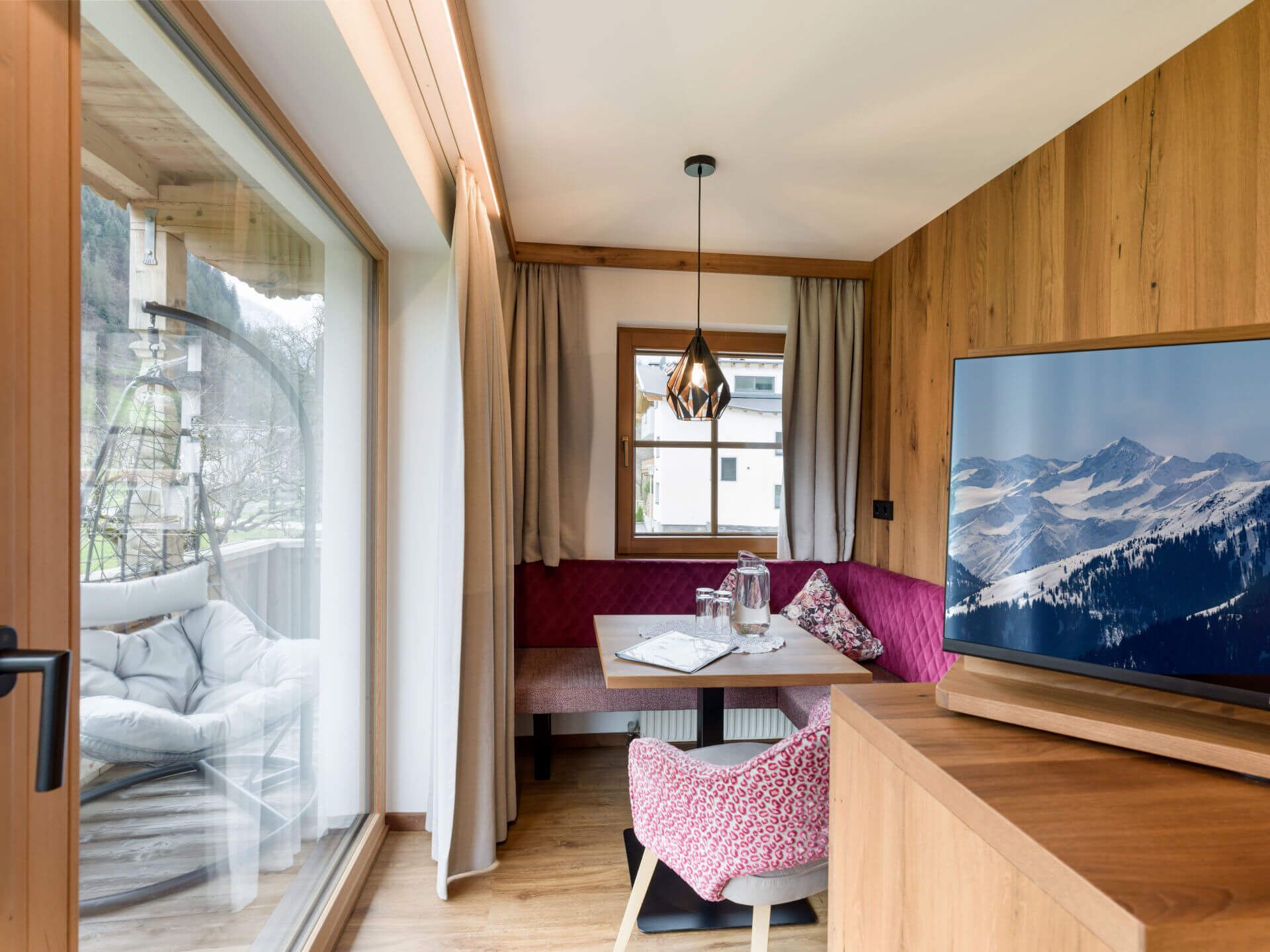A modern room with a large TV, wooden walls, a dining area, and a view of mountains.