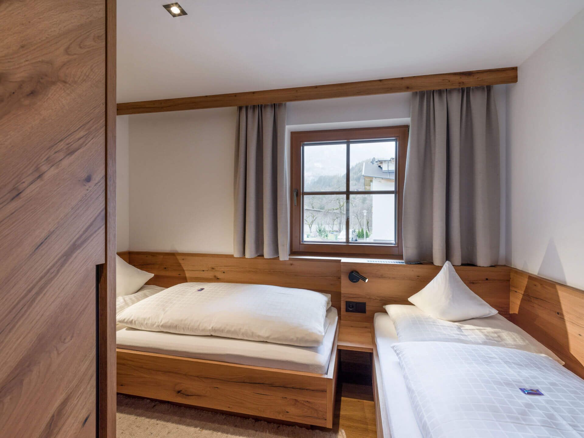 Ein Schlafzimmer mit zwei Holzbett, einem Fenster mit Vorhängen und Blick ins Freie.