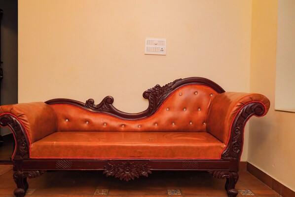 A brown leather sofa with ornate carvings and a tufted backrest against a plain wall.