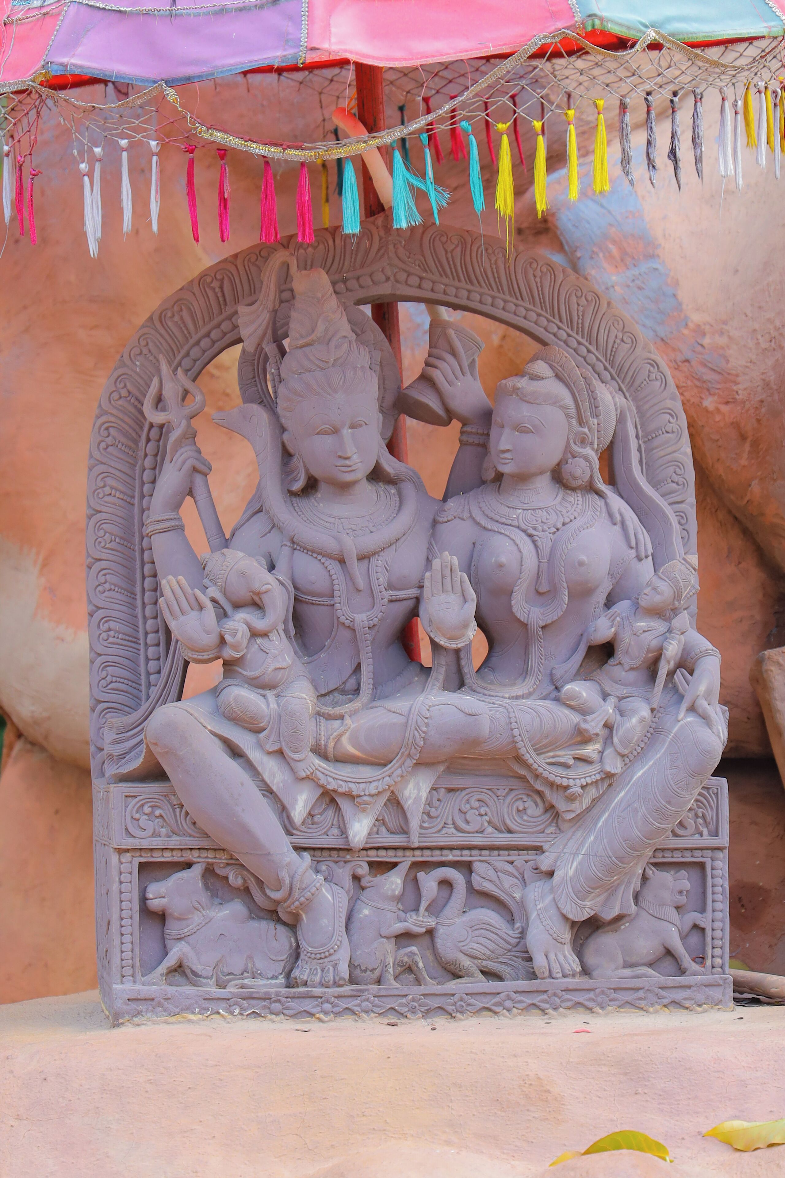 A detailed stone sculpture of deities with intricate carvings and a decorative arch.