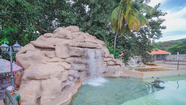 A rock formation with a waterfall, a pool, and a dolphin. - Mount Retreat (Madurai)