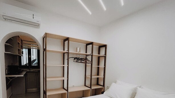 A hotel room with a bed, a wardrobe with multiple shelves, and a desk with a chair. - Venetian Vicolo by Corfu Escapes  (Corfu)