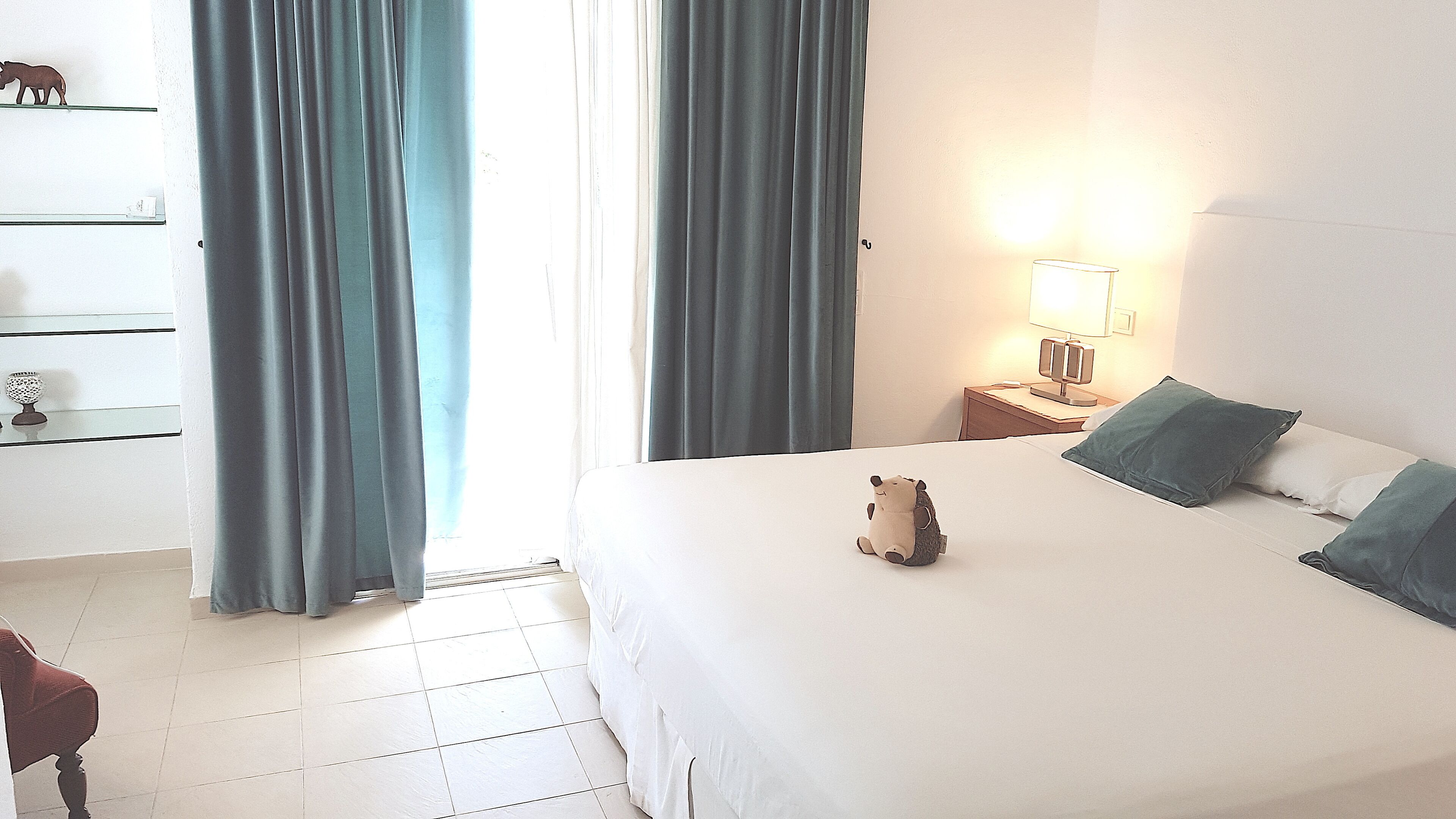 A hotel room with a bed, a nightstand with a lamp, a dresser, and a chair.