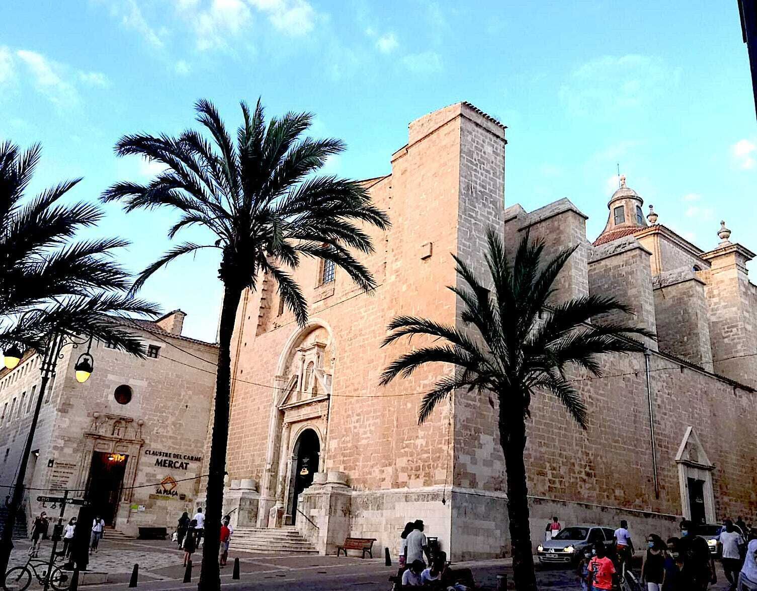 A historic building with a prominent entrance, palm trees, and a clear sky.
