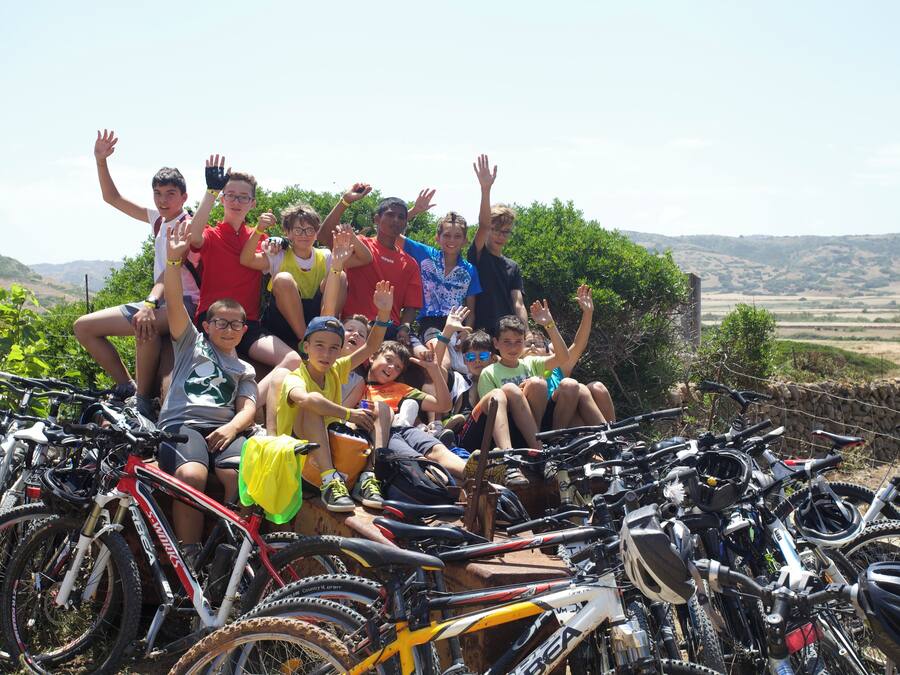 Un grupo de personas posando con bicicletas en un entorno exterior soleado.