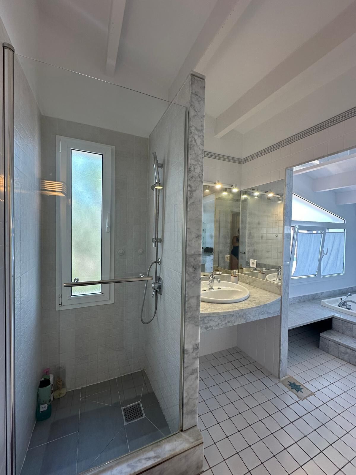 A modern bathroom with a glass-enclosed shower, a large mirror, and a marble countertop.