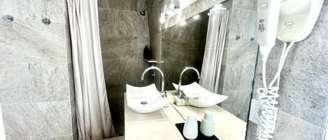 Casa de banho moderna com um espelho grande, duas pias, zona de duche e um secador de cabelo fixado na parede.