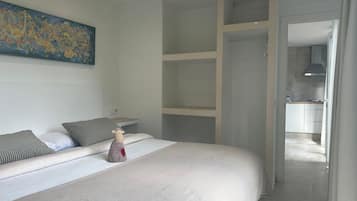 A modern bedroom with a large bed, a painting on the wall, and a view into the kitchen.