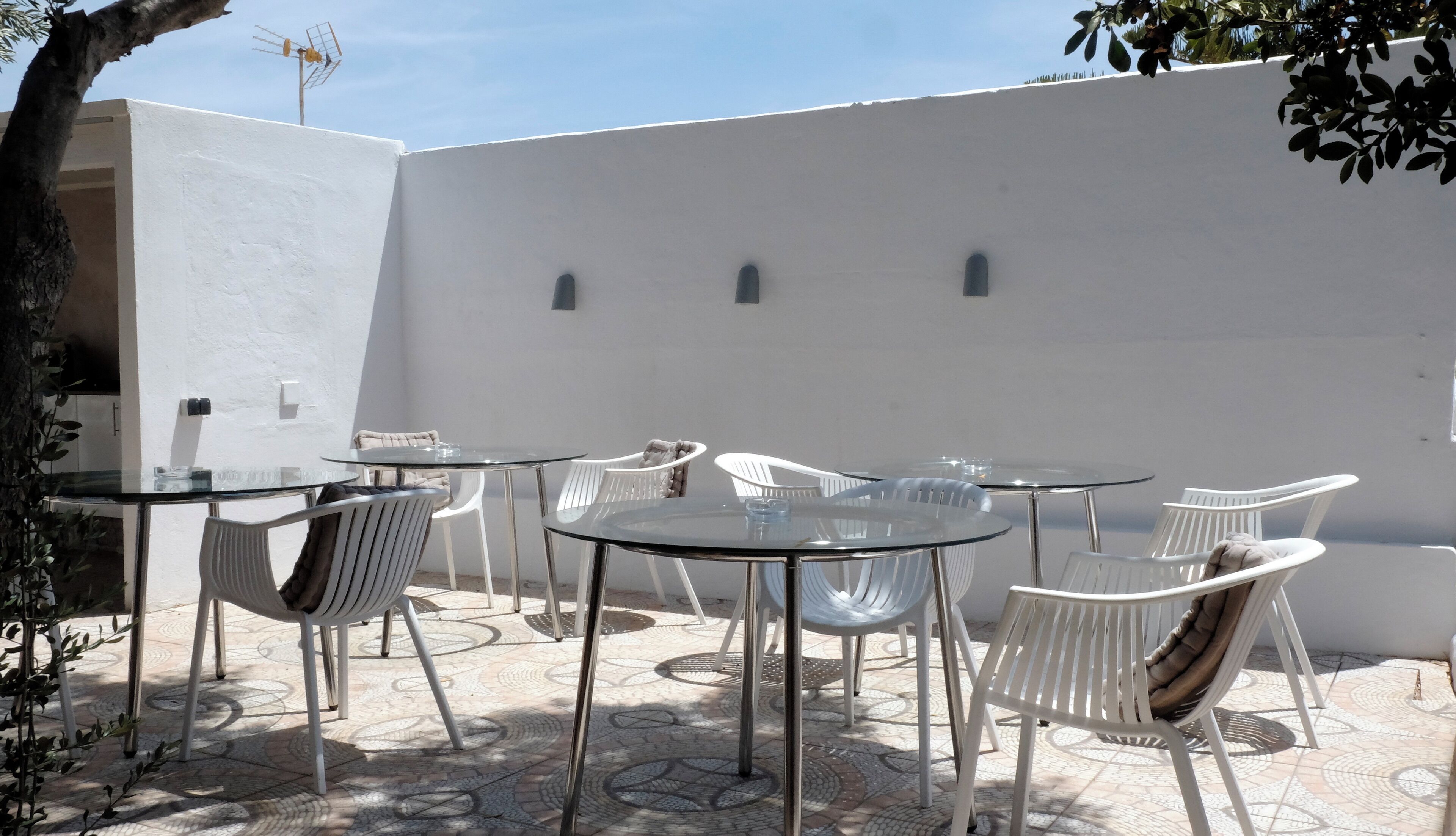 Un espace patio aménagé avec plusieurs tables rondes en verre et des chaises en plastique blanches.