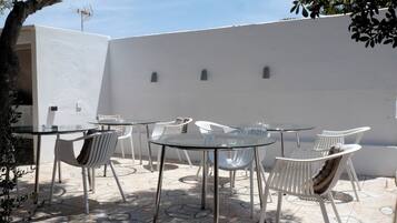 Un espace patio aménagé avec plusieurs tables rondes en verre et des chaises en plastique blanches.