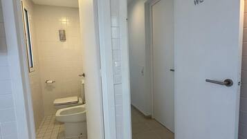 A bathroom with white tiled walls and floor, a toilet, and a shower.