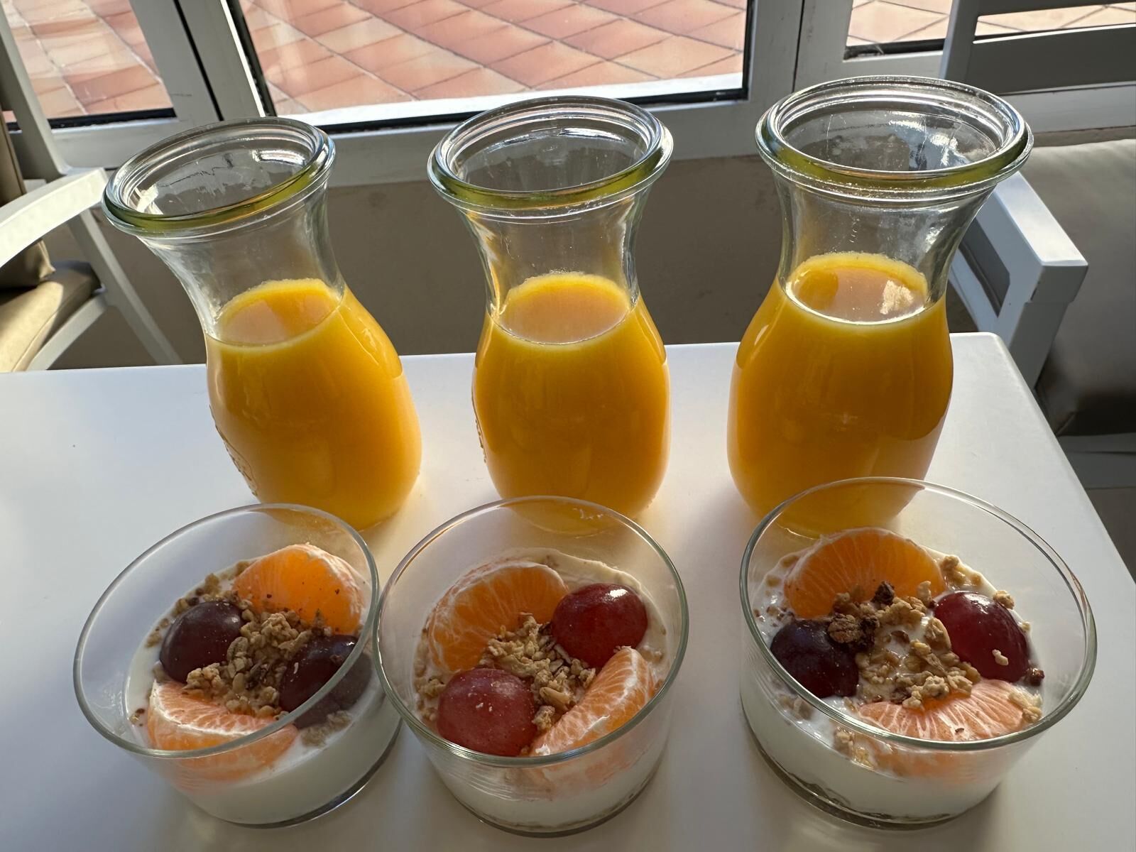 Tres botellas de jugo de naranja y tres tazones de ensalada de frutas con granola.
