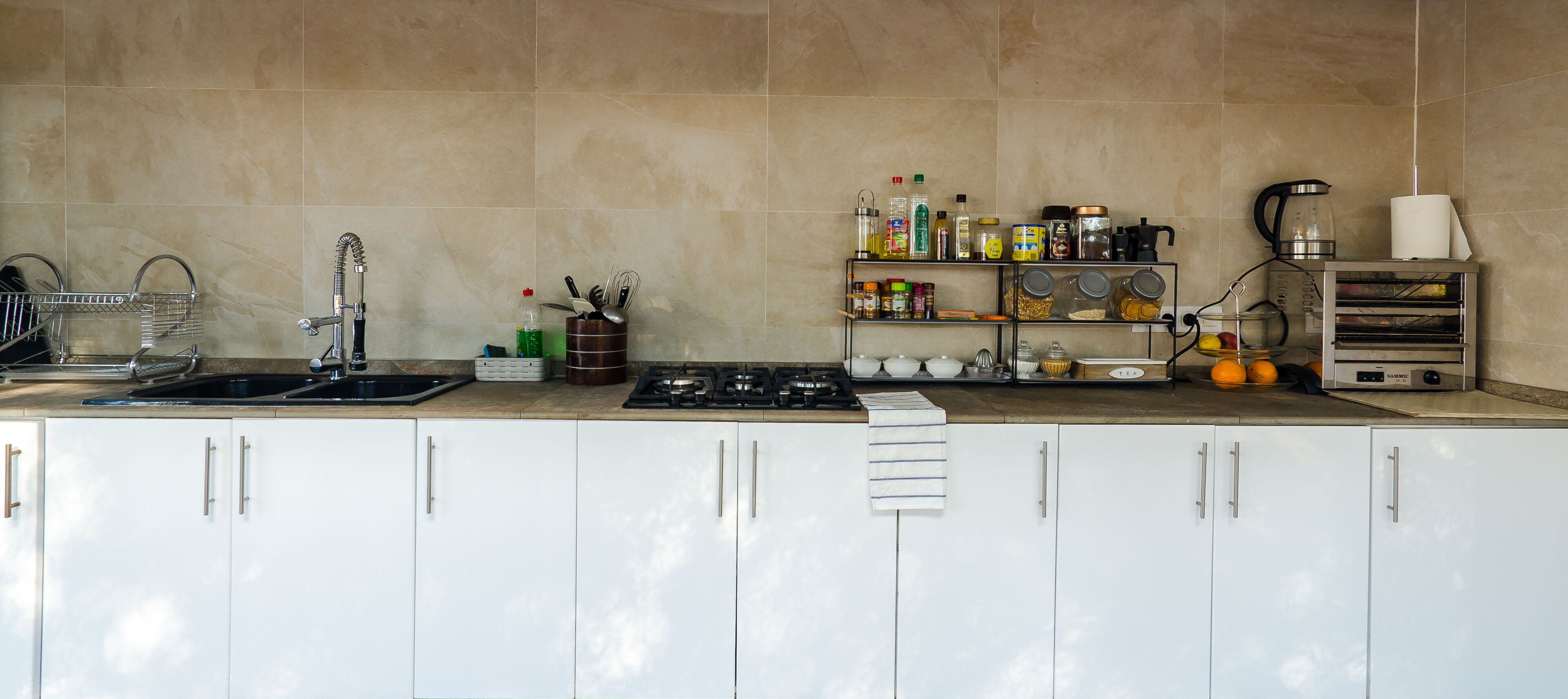 A kitchen with a gas stove, sink, and various kitchen appliances. There are cabinets, a shelf with kitchen items, and a countertop.