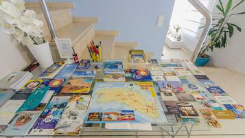 A glass table with various travel brochures and a map, surrounded by a staircase and potted plants.