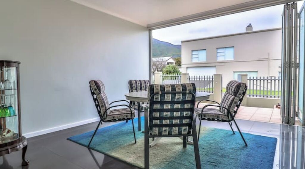 A modern dining area with a round table and four chairs, a glass cabinet, and a view of a building and mountains through large windows.