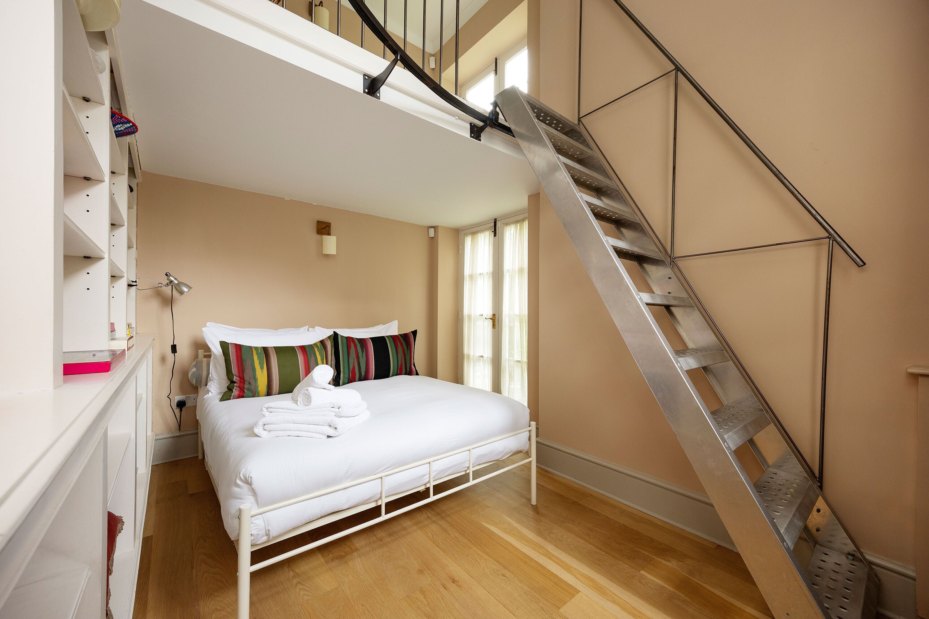 A bedroom with a bed, a white wardrobe, a staircase, and a window.