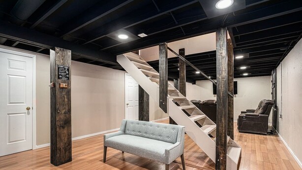 A spacious room with a wooden staircase, a grey sofa, and a massage chair.