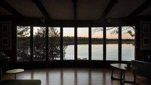 Habitación con ventanas amplias con vista a un lago, suelo de madera y muebles escasos.