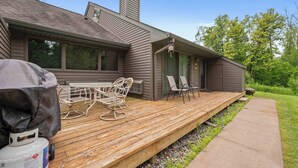 Una casa moderna con terraza de madera, dos sillas y una parrilla.