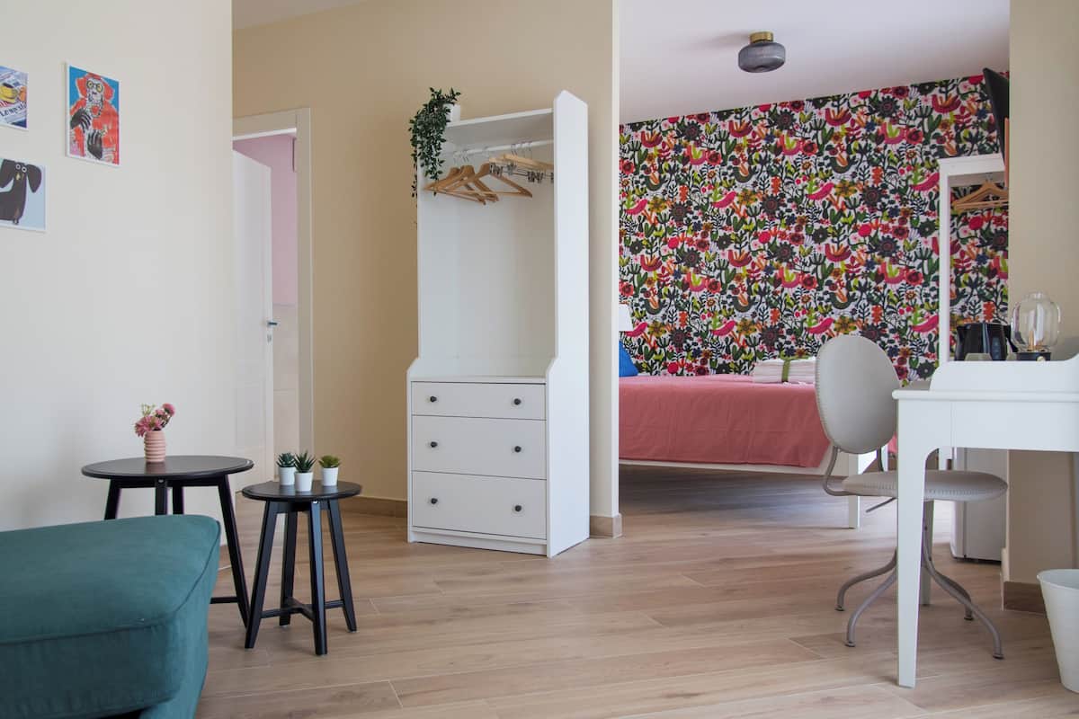 A room with a bed, a desk, a chair, a wardrobe, and a small table with plants.