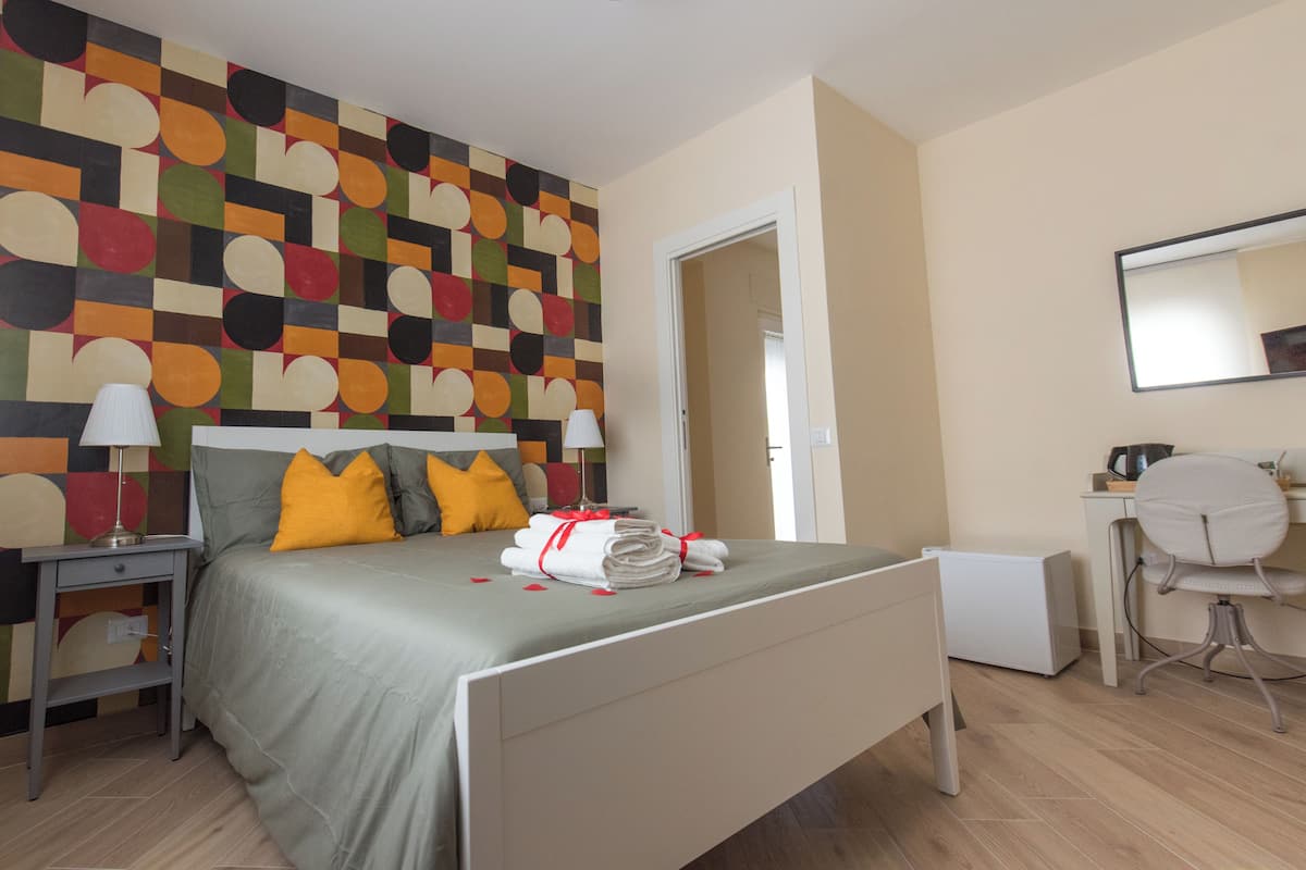 A hotel room with a bed, bedside table, lamp, and a desk with a chair.