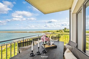 A balcony with a table set for dining, overlooking a coastal view.