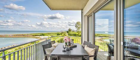 A balcony with a table set for dining, overlooking a coastal landscape.