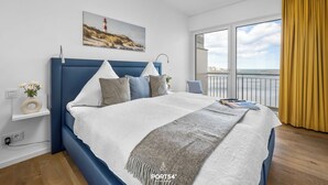 Een moderne slaapkamer met een groot bed, uitzicht op zee en een schilderij van een vuurtoren.