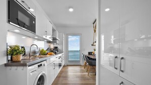 Een moderne keuken met een wasmachine, een spoelbak en een eethoek met uitzicht op zee.
