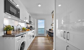 A modern kitchen with a washing machine, a sink, and a dining area with a view of the sea.