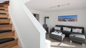 A modern living room with a staircase, a sofa set, a coffee table, and a painting of a beach scene.
