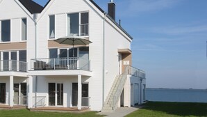 A two-story white building with a balcony, a staircase, and a view of the water.