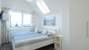 A bedroom with a bed, a TV, a window with curtains, a skylight, and a painting on the wall.