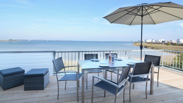 An outdoor dining area with a table, chairs, and an umbrella overlooking a body of water.