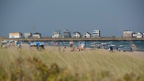 A beach with beach chairs and umbrellas, a lifeguard tower, and houses along the shore.