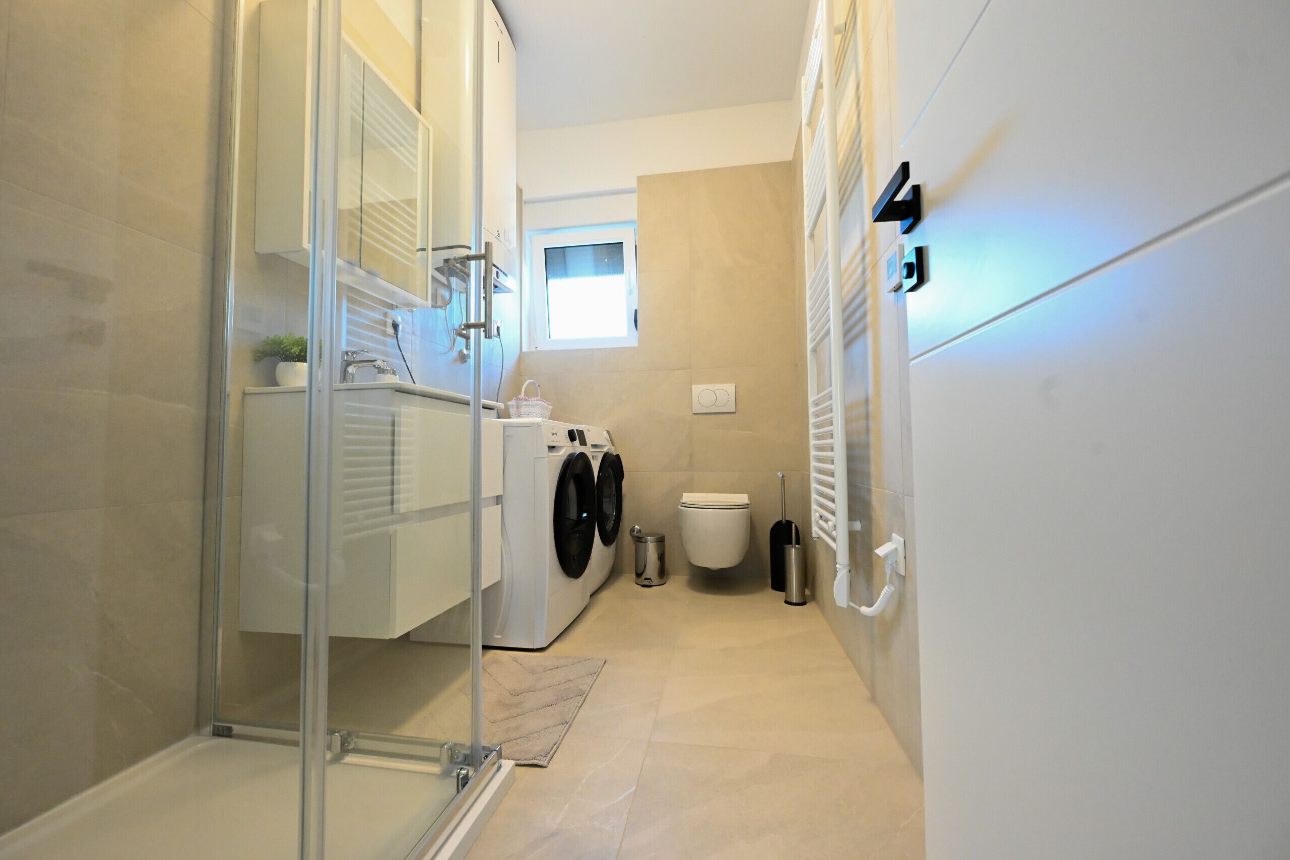A compact bathroom with a glass shower enclosure, a washing machine, a toilet, and a towel rack.