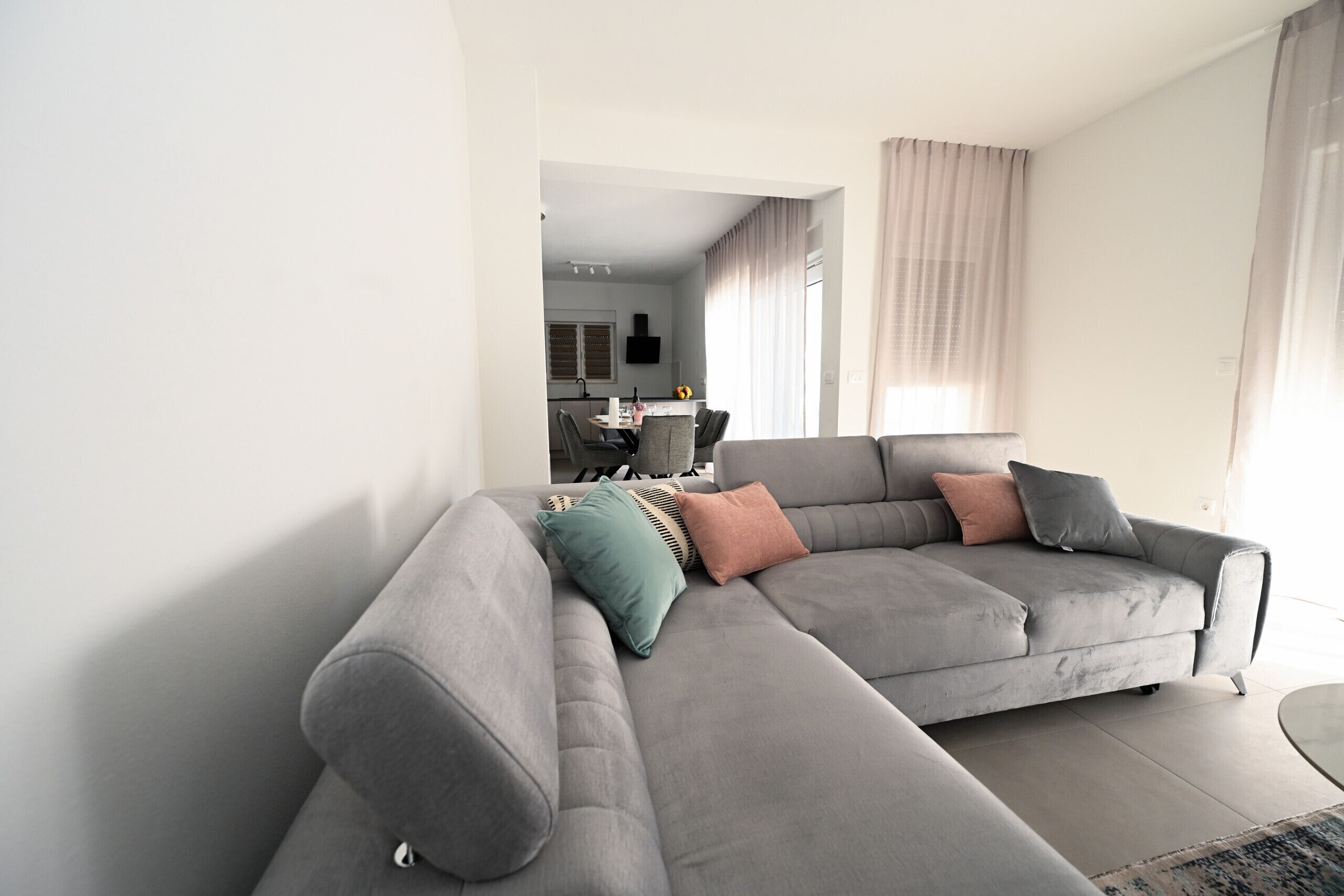 Een moderne woonkamer met een grijze modulaire bank, een eettafel en een keuken op de achtergrond.