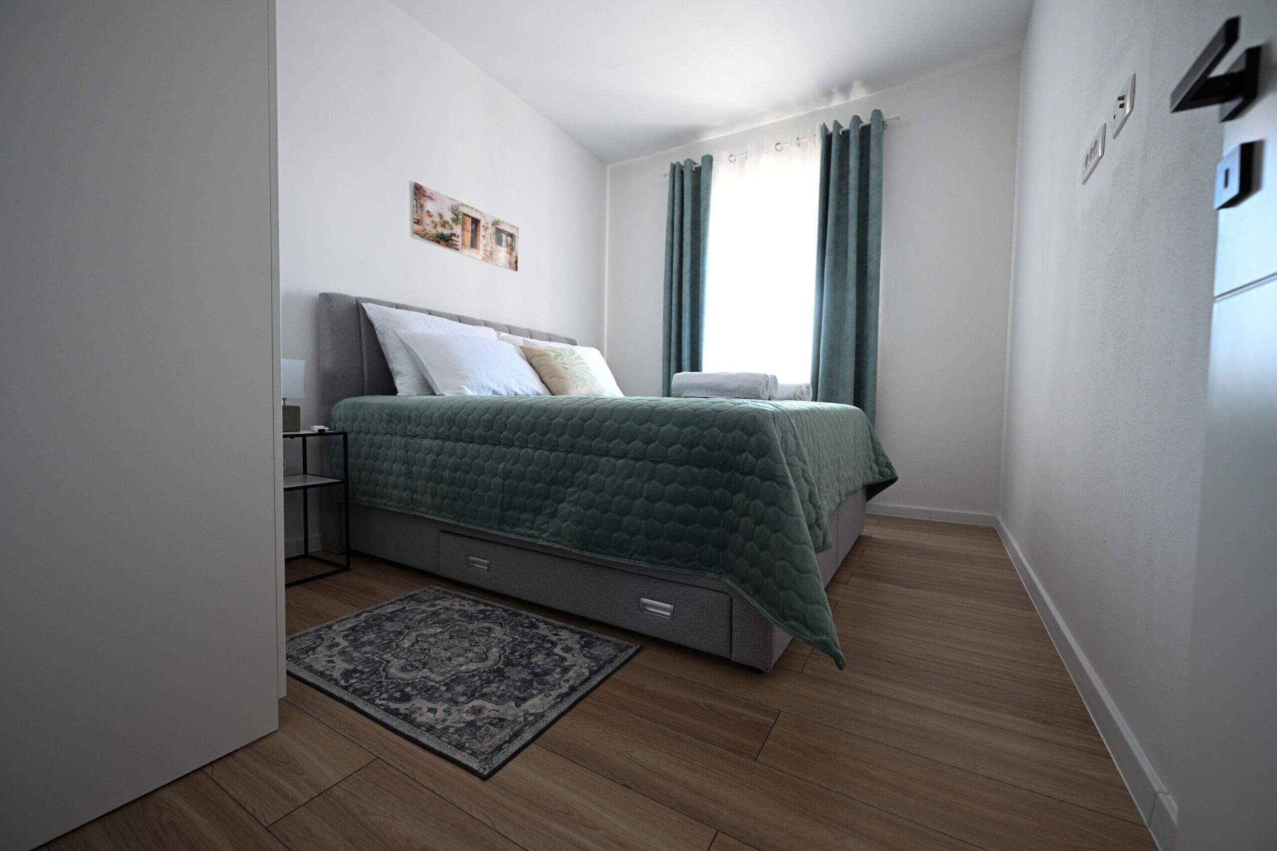 A modern bedroom with a bed, a nightstand, a wall-mounted artwork, and a window with curtains.