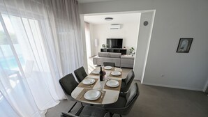 A dining area with a table set for six, a sofa in the background, and a TV mounted on the wall. - Beautiful Villa Zara Blu with pool (Briševo)