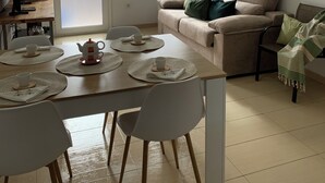 A living room with a beige sofa, a dining table with placemats and a teapot, a coffee table, and a decorative branch on the wall. - SAND AND SALT, terrace 25 mts, air conditioning and direct access to the pool. (deltebre)