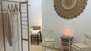 A room with a wooden clothes rack, a woven wall hanging, two white chairs, a small table with a candle, and a basket on a shelf. - SAND AND SALT, terrace 25 mts, air conditioning and direct access to the pool. (deltebre)