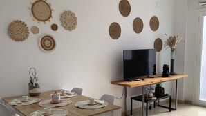 A dining area with a wooden table set for four, white chairs, and a TV on a stand in the background. - SAND AND SALT, terrace 25 mts, air conditioning and direct access to the pool. (deltebre)