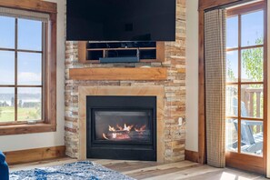 A fireplace with a TV above it, a stone wall, and a view of the outdoors. - Osprey's Penthouse|Exclusive Tamarack Perks (Tamarack)