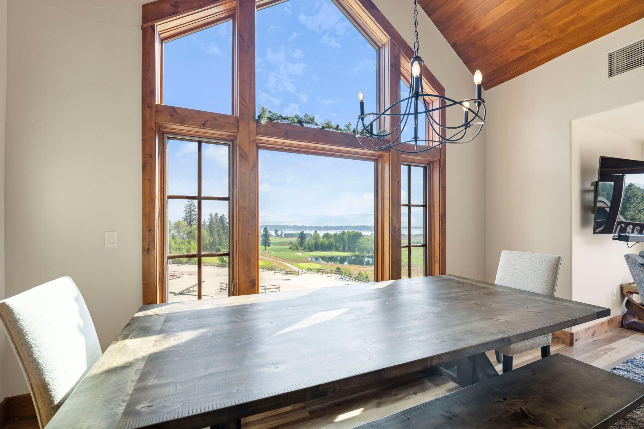 A dining area with a large table, wooden beams, and a view of a landscape through large windows.