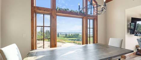 A dining area with a large table, wooden beams, and a view of a landscape through large windows.
