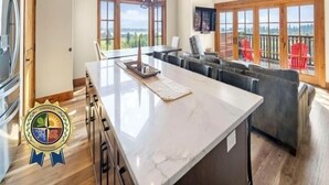Une cuisine spacieuse dotée d’un grand îlot central, de poutres apparentes en bois au plafond et de grandes fenêtres offrant une vue sur l’extérieur.